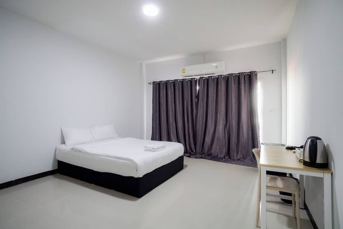 A bedroom with a bed, a desk, a chair, an air conditioning unit, and a window with curtains.