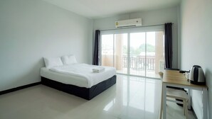 A hotel room with a bed, a desk, a chair, an air conditioner, and a view of the outdoors. - NP Place Santitham (Chiang Mai)
