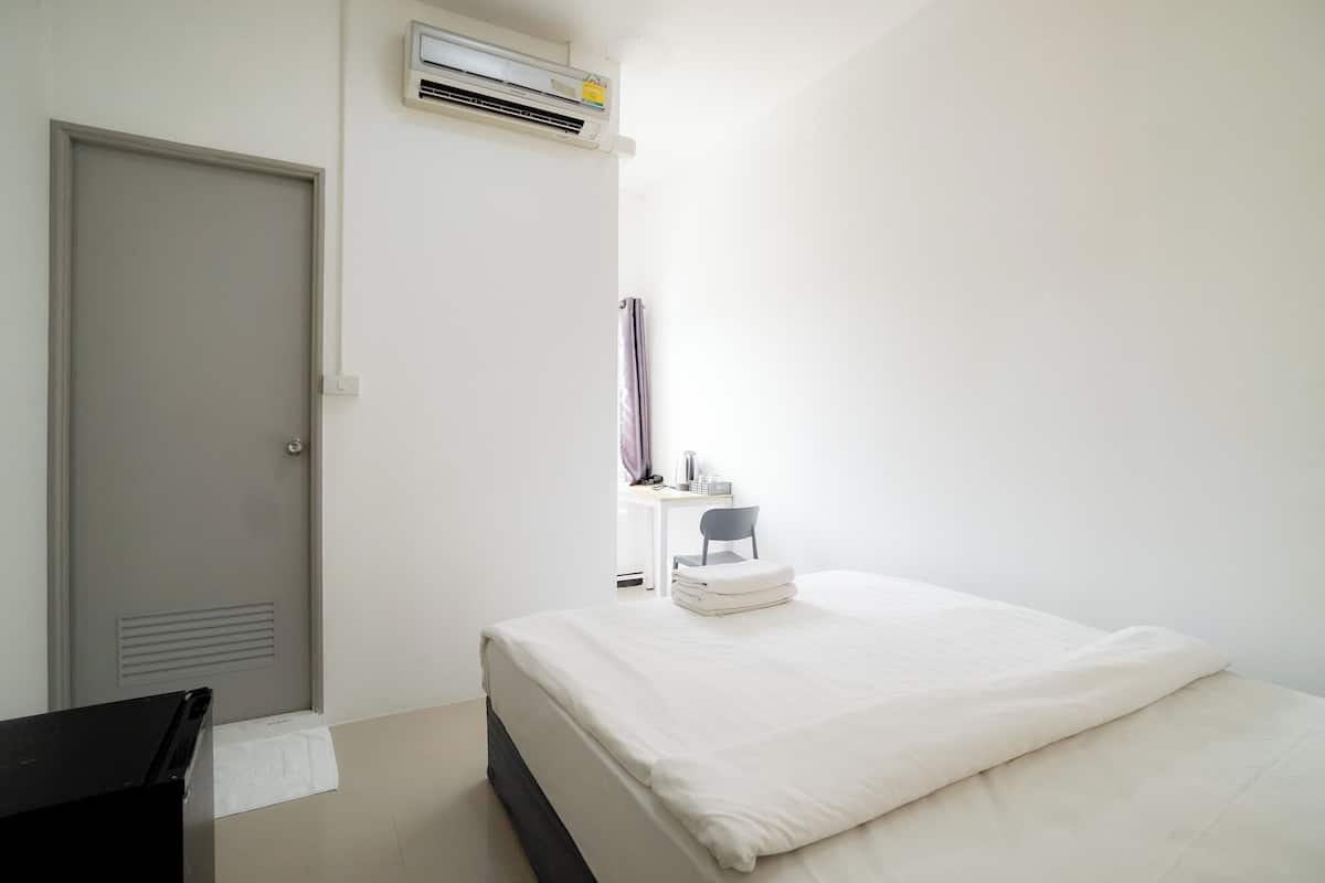 A bedroom with a bed, a desk, a chair, and an air conditioning unit.