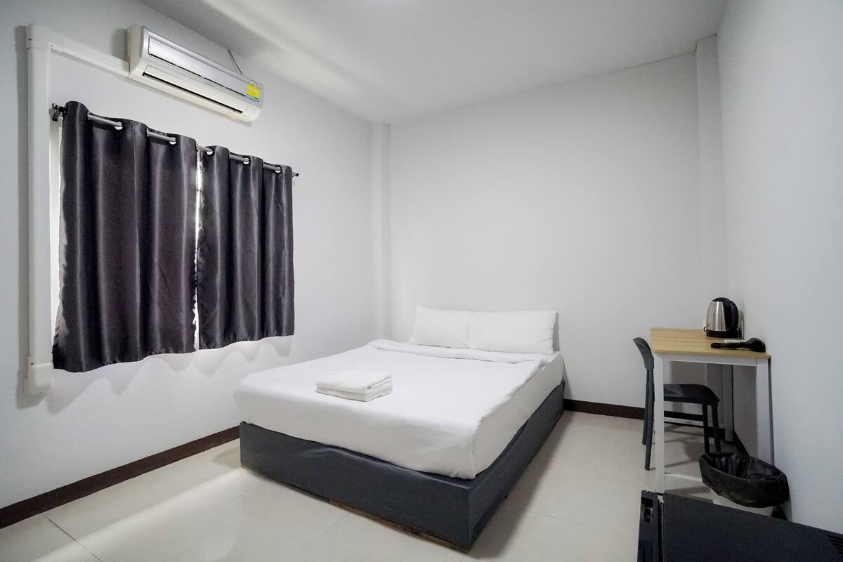 A bedroom with a bed, a desk, a chair, and an air conditioning unit.