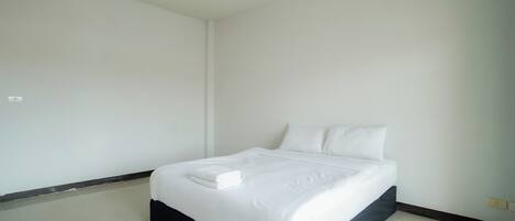 A clean, minimalist bedroom with a large bed, white bedding, and a dark-colored headboard.