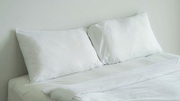 A bed with white bedding and pillows against a plain wall. - NP Place Santitham (Chiang Mai)