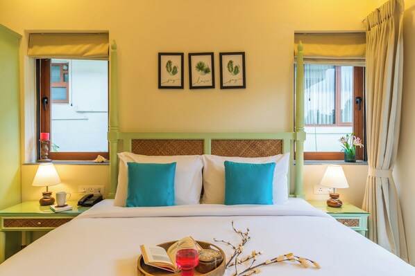 Une chambre d’hôtel comprenant un lit, deux tables de chevet avec des lampes, une fenêtre avec des rideaux et des œuvres d’art murales.