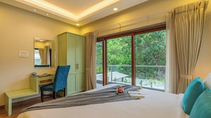 A hotel room with a bed, a desk, a chair, a mirror, and a balcony with a view of greenery. - ELIVAAS Azalea 3 BHK with Pvt Pool (Siolim)