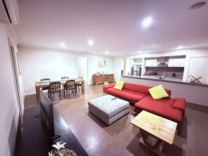 A modern living room with a red sofa, grey ottoman, and a wooden coffee table. - 4Bedroom Bungalow in Williams Landing (Williams Landing)