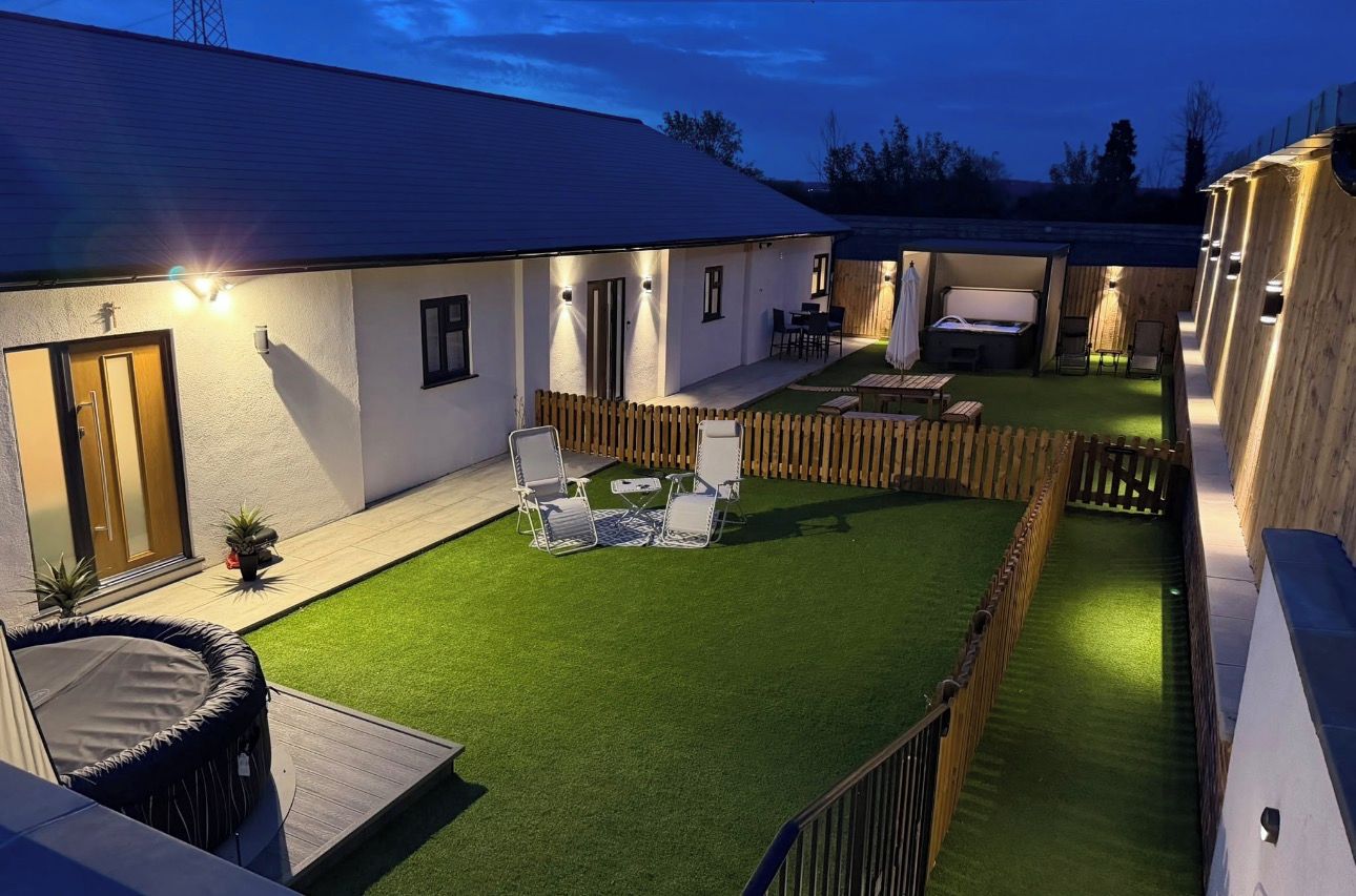 A well-lit outdoor area with a wooden deck, a small pool, and a seating area with chairs and a table.