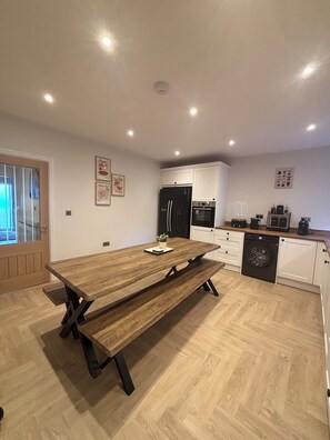 Une cuisine moderne avec une table à manger en bois, des appareils électroménagers intégrés et une vue à travers une porte vitrée.