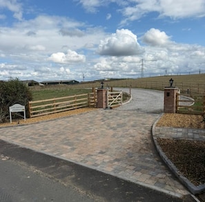 A gated entrance to a farm with a paved driveway and a wooden fence.