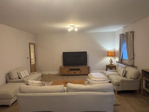 Un soggiorno con una TV a schermo piatto su un supporto in legno, due divani, un tavolino, una lampada e una libreria.