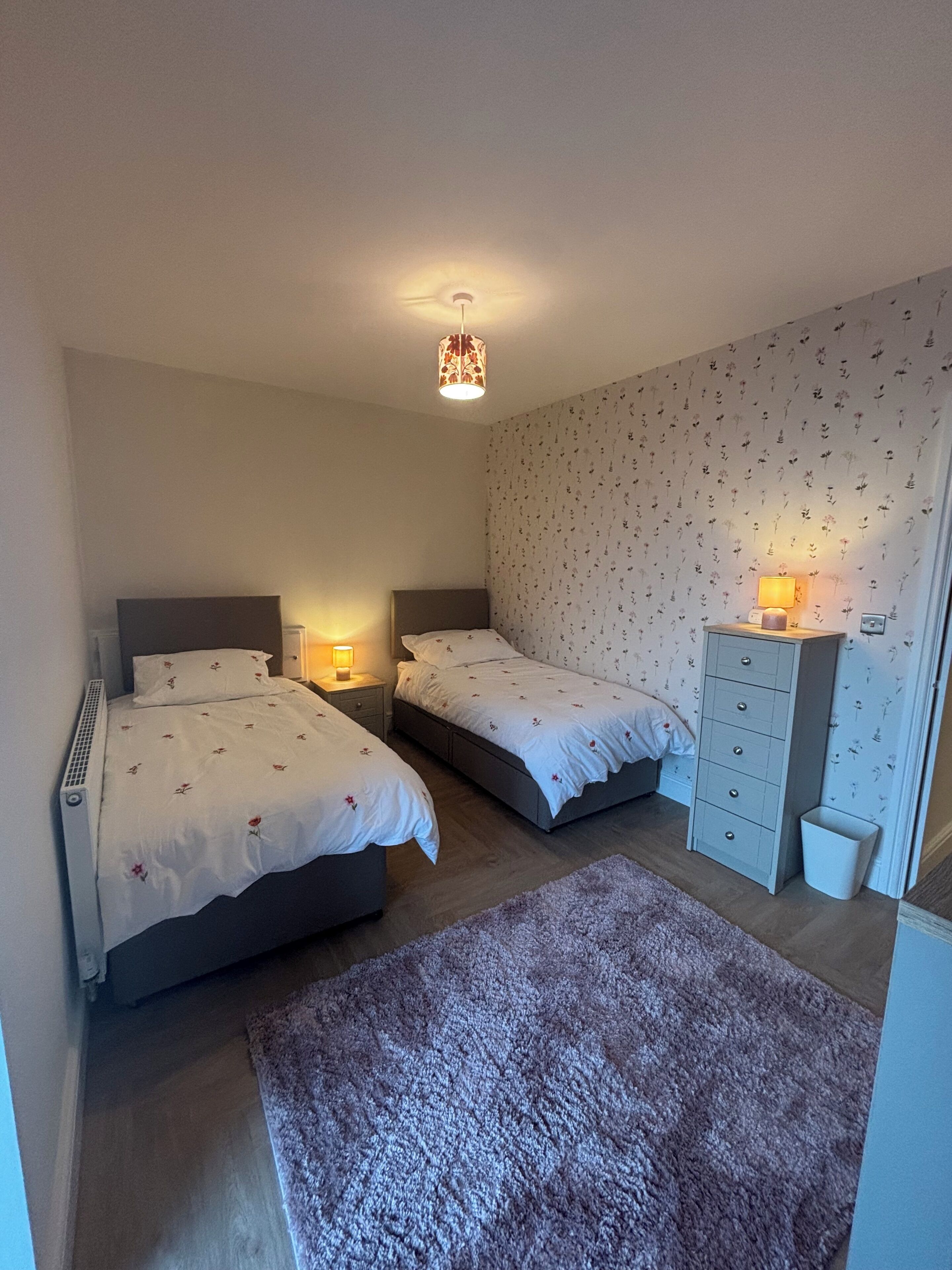 Ein Schlafzimmer mit zwei Betten, einem Schminktisch, einem Heizkörper und einer Wand mit Muster.