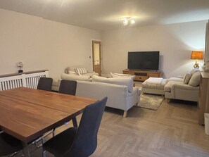 A living room with a wooden dining table, two sofas, a TV, and a lamp.