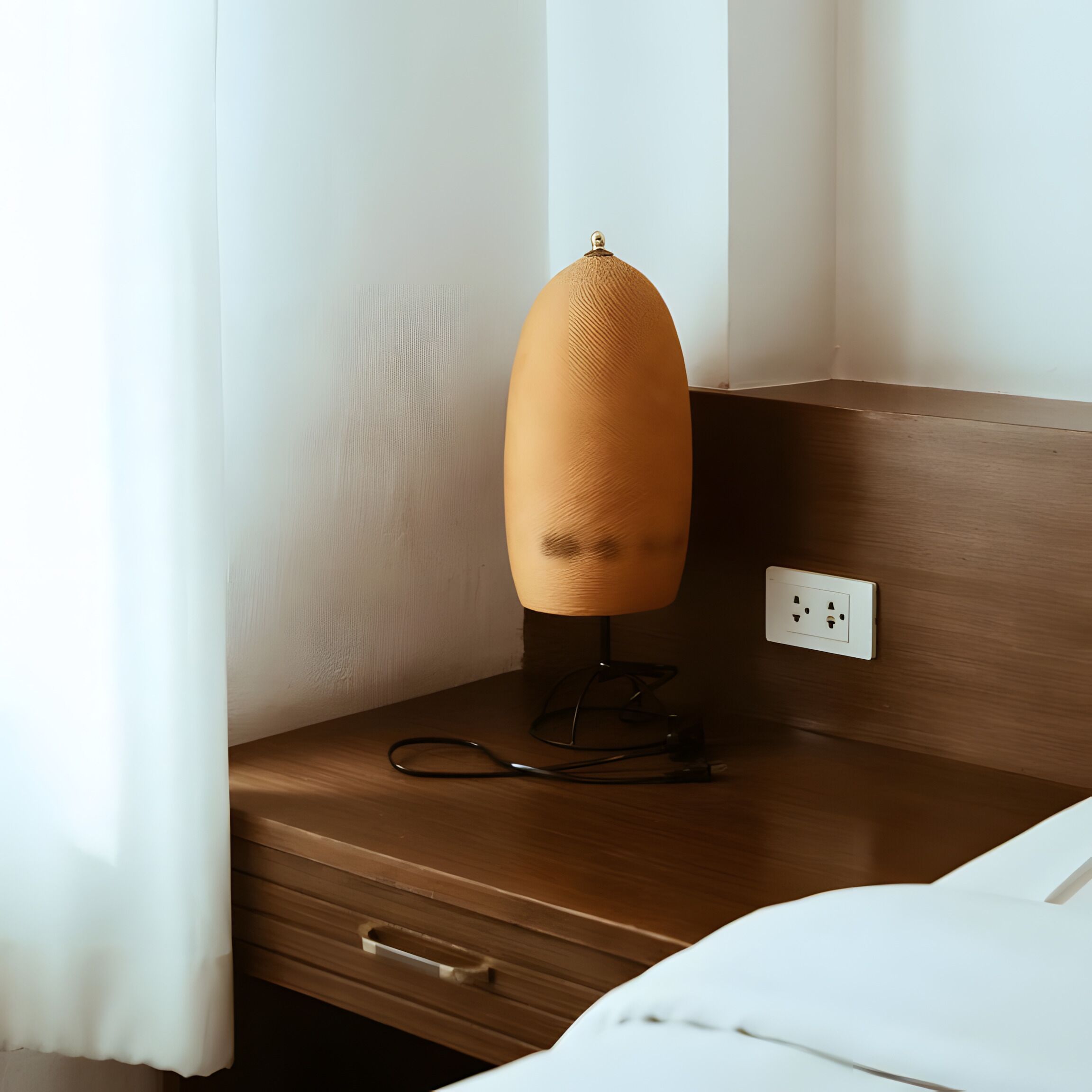 A wooden bedside table with a lamp, a power outlet, and a drawer.