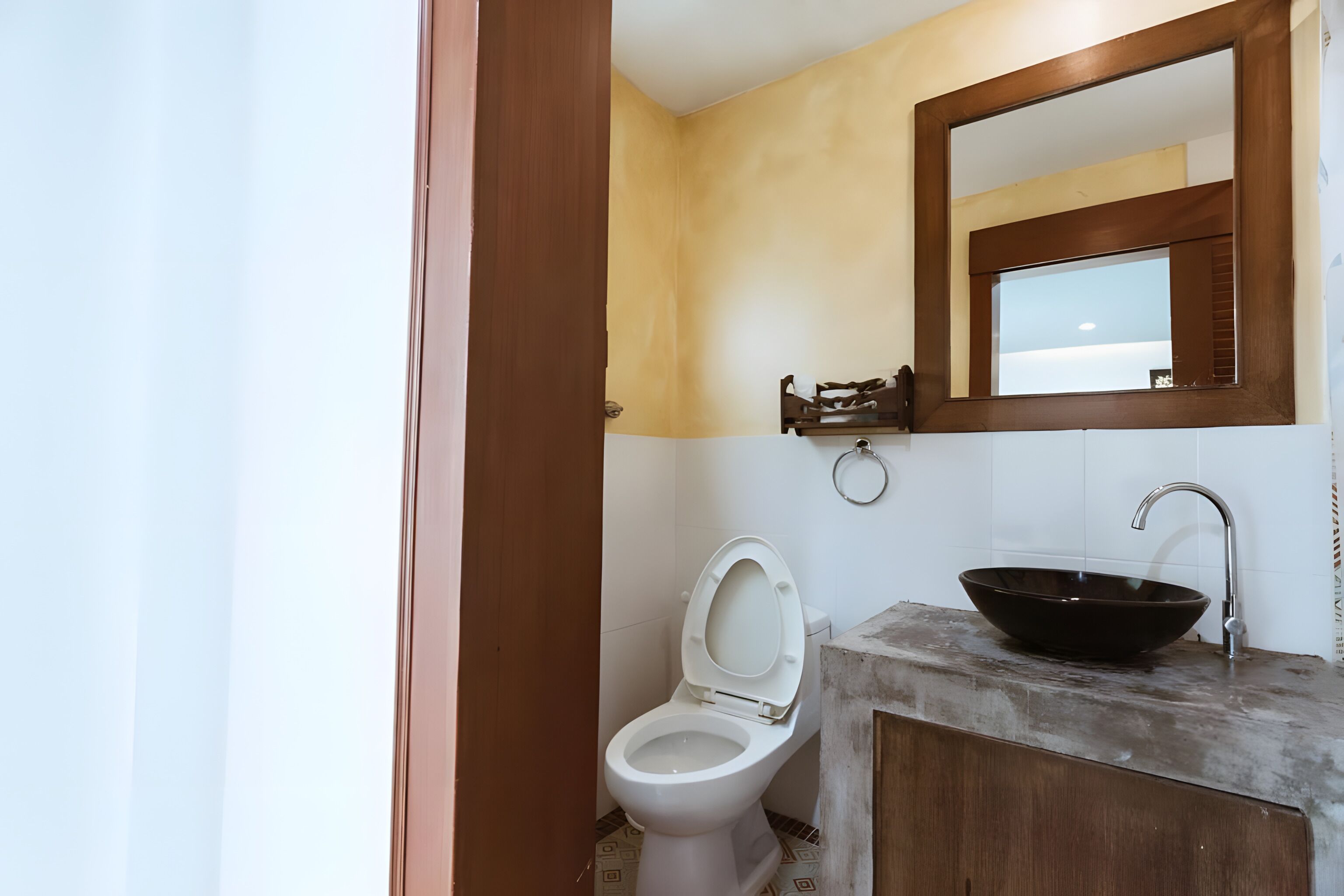 Ein Badezimmer mit Toilette, einem hölzernen Waschtisch mit schwarzem Becken und einem Spiegel über dem Waschtisch.