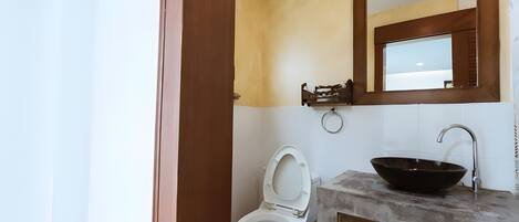 A bathroom with a toilet, a wooden vanity with a black sink, and a mirror above the vanity.