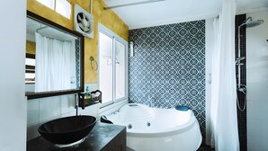 A bathroom with a bathtub, a large mirror, a black sink basin, and patterned tiles. - Snap Inn Thaphae (Chiang Mai)