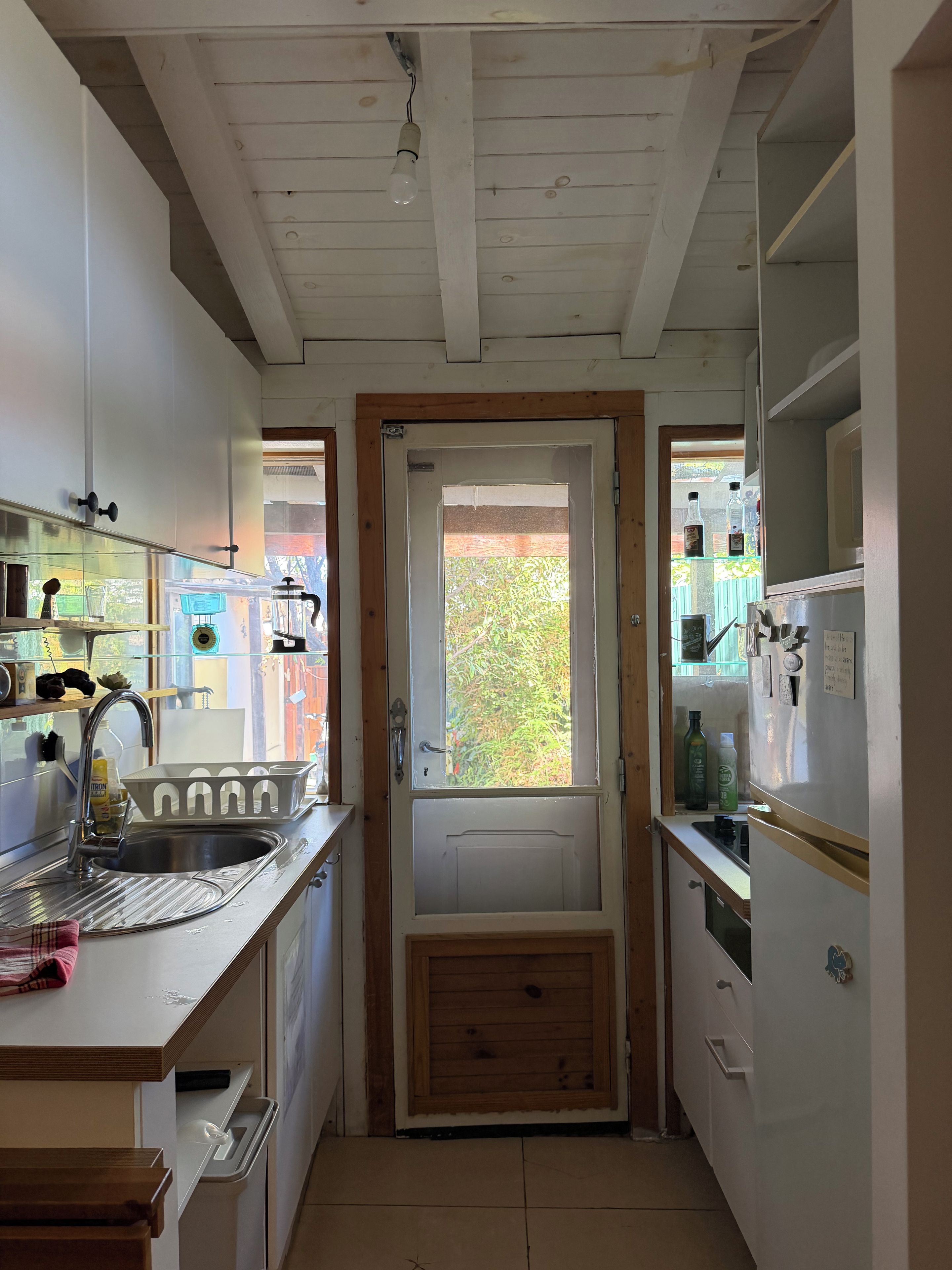 Eine schmale Küche mit Holztür, Edelstahlspüle und Kühlschrank.