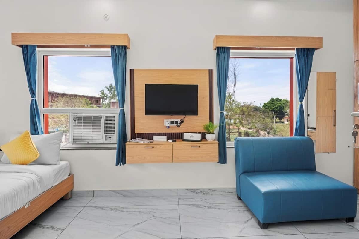 A modern room with a bed, a blue sofa, a TV mounted on a wooden wall, and a window with curtains.