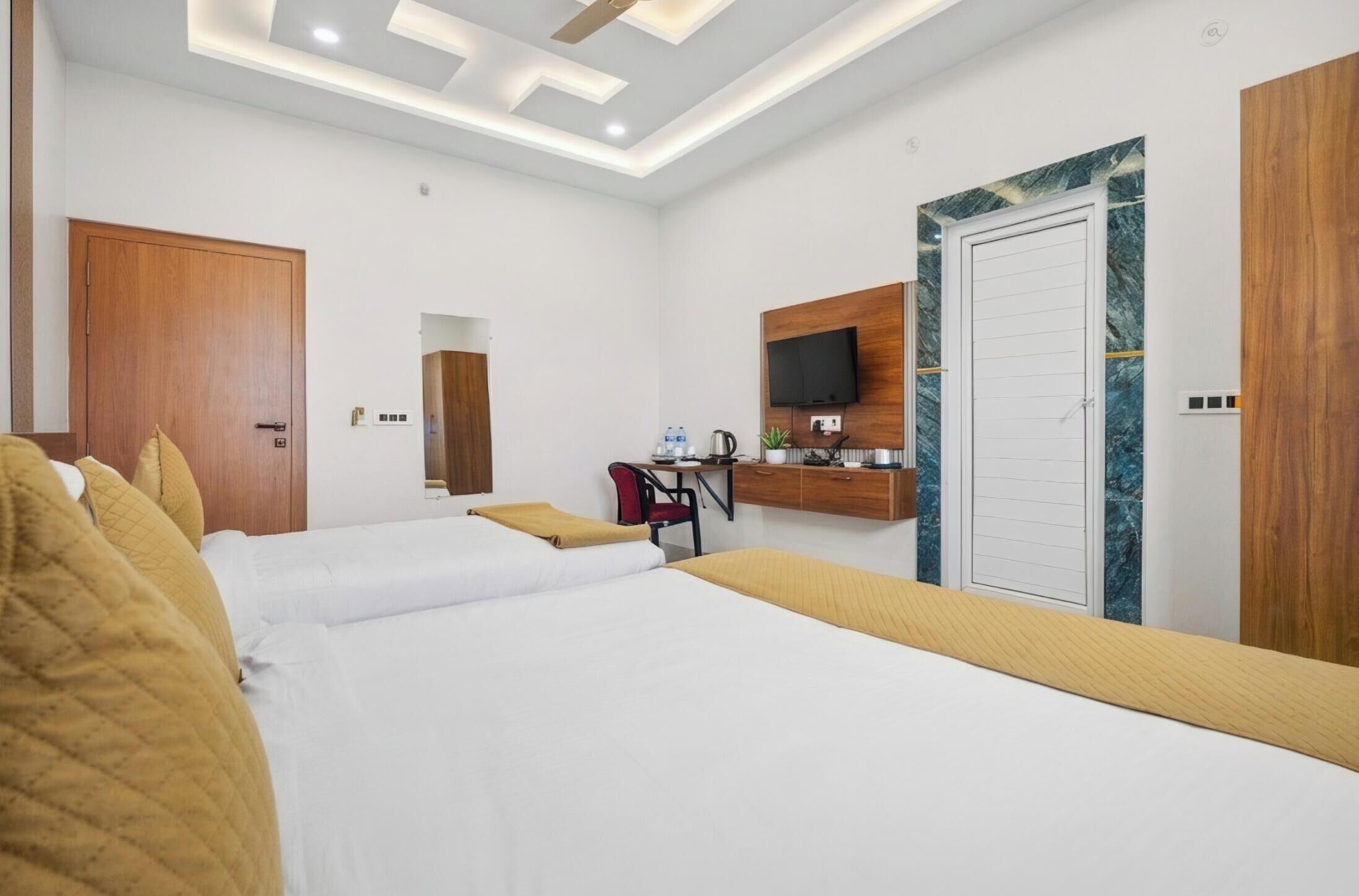 A hotel room with two beds, a desk with a chair, a TV mounted on the wall, and a wooden wardrobe.