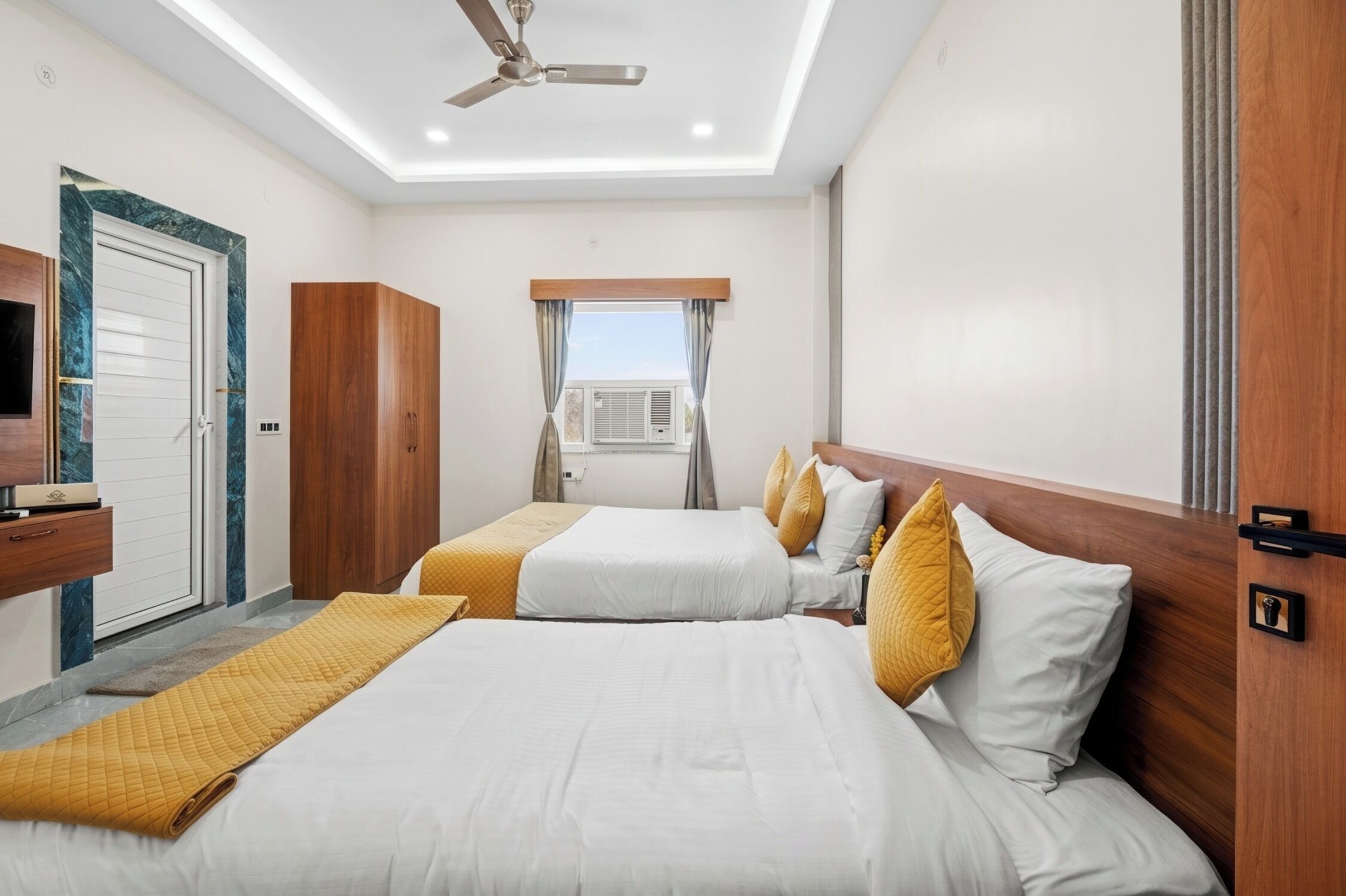 Habitación de hotel con dos camas, ventilador de techo, equipo de aire acondicionado y armario de madera.