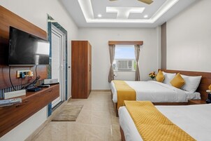 A hotel room with a TV, wooden furniture, a bed with yellow bedding, and a window with curtains.