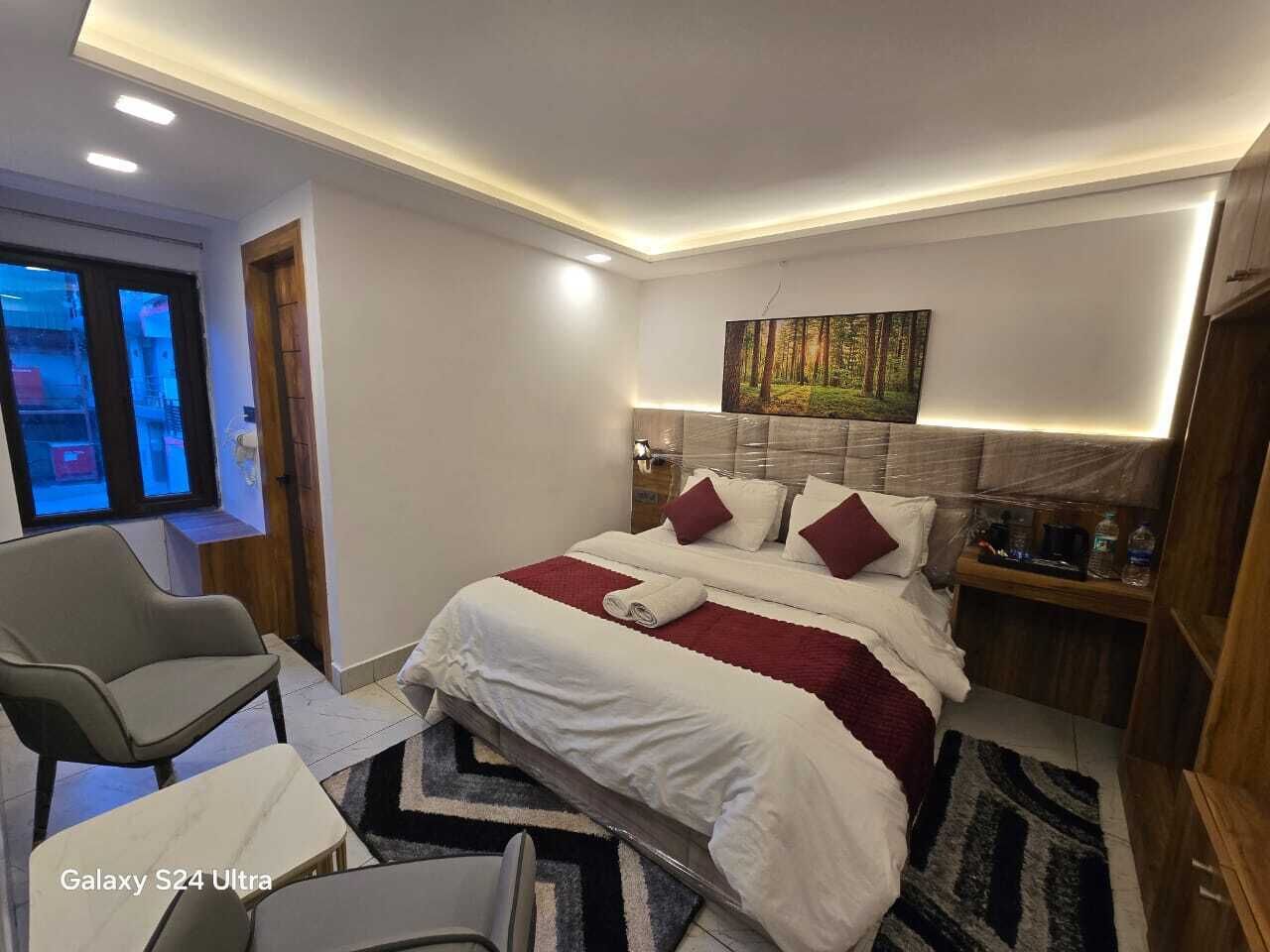 A modern hotel room with a neatly made bed, a chair, a nightstand, and a painting on the wall.