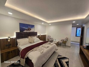 Ein modernes Hotelzimmer mit einem großen Bett, einem Nachttisch, einem Sessel, einem kleinen Tisch und einem Fernseher.