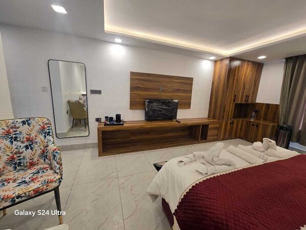 A modern hotel room with a wooden vanity, a flat-screen TV, a large mirror, and a floral-patterned sofa.