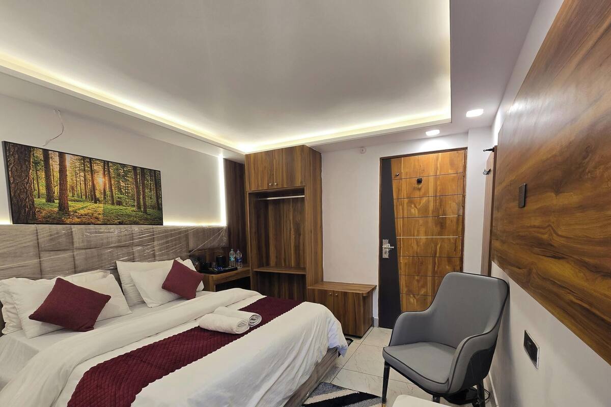 A neatly arranged bedroom with a bed, a chair, a wardrobe, and a painting on the wall.