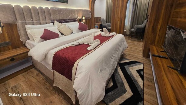 Een kamer met een Galaxy S24 Ultra, een bed, houten lambrisering, een televisie en een schilderij aan de muur.