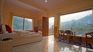 Una camera da letto con un letto, una scrivania, una sedia e un balcone che si affaccia sulle colline.