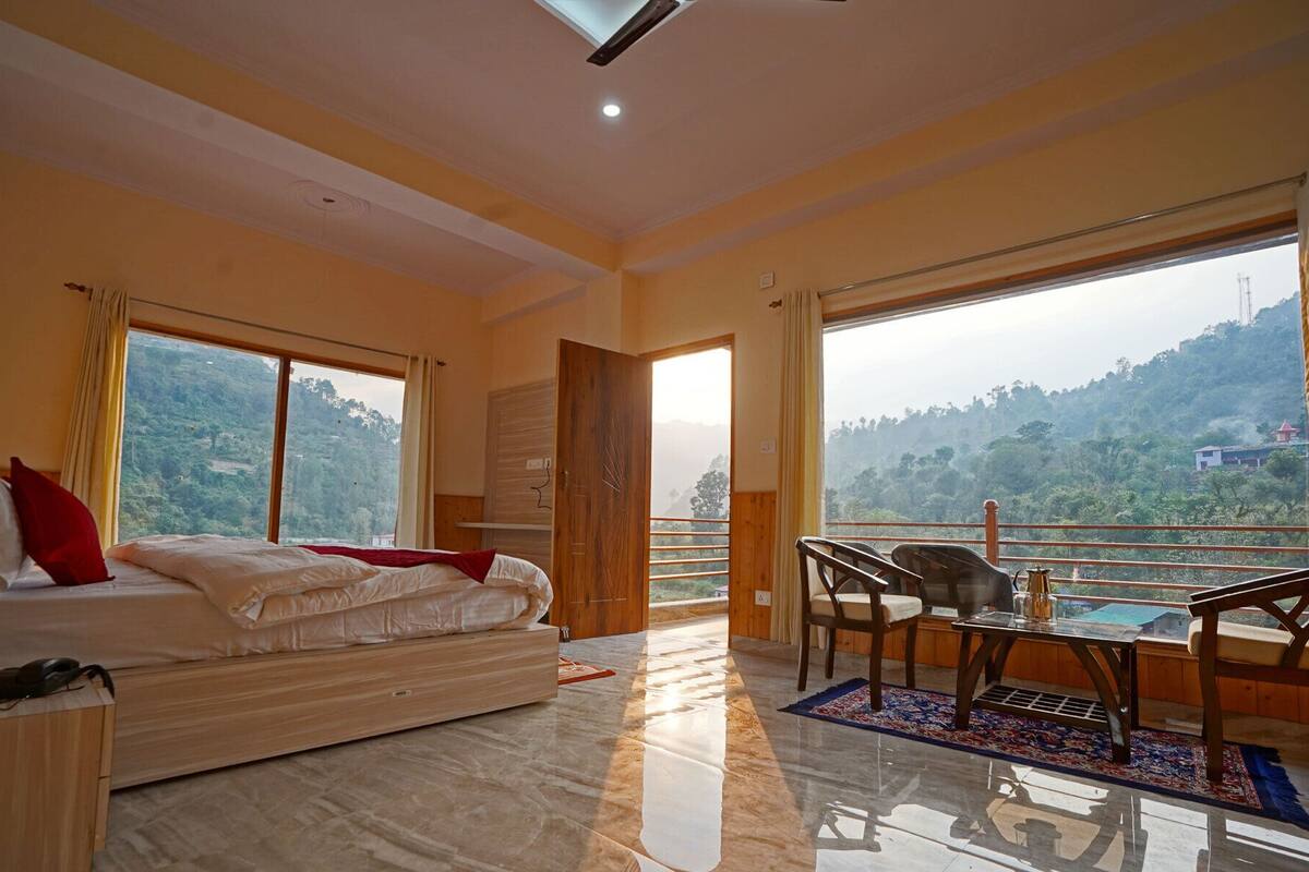 A bedroom with a bed, a desk, a chair, and a balcony with a view of the hills.