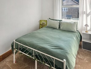A bed with a metal frame, a green bedspread, and a window with a view of a building. - 3 bedroom accommodation in Redruth (Redruth)
