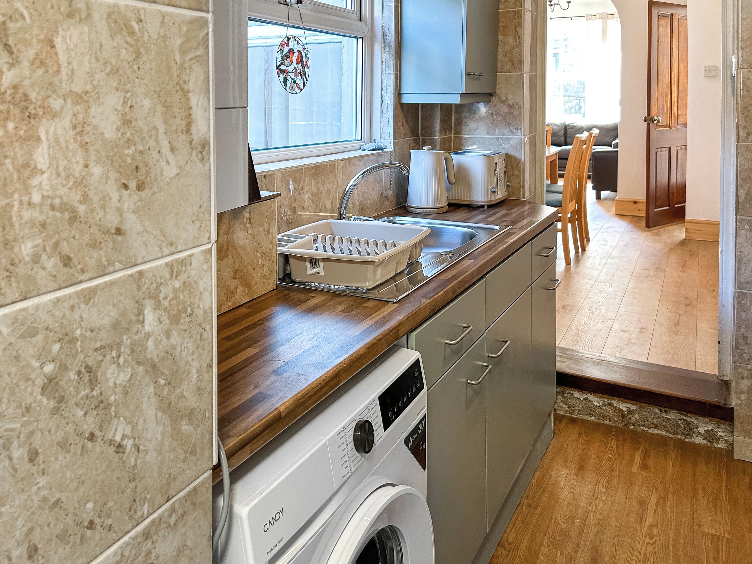 A compact kitchen with a washing machine, a sink, and a window with a decorative item.