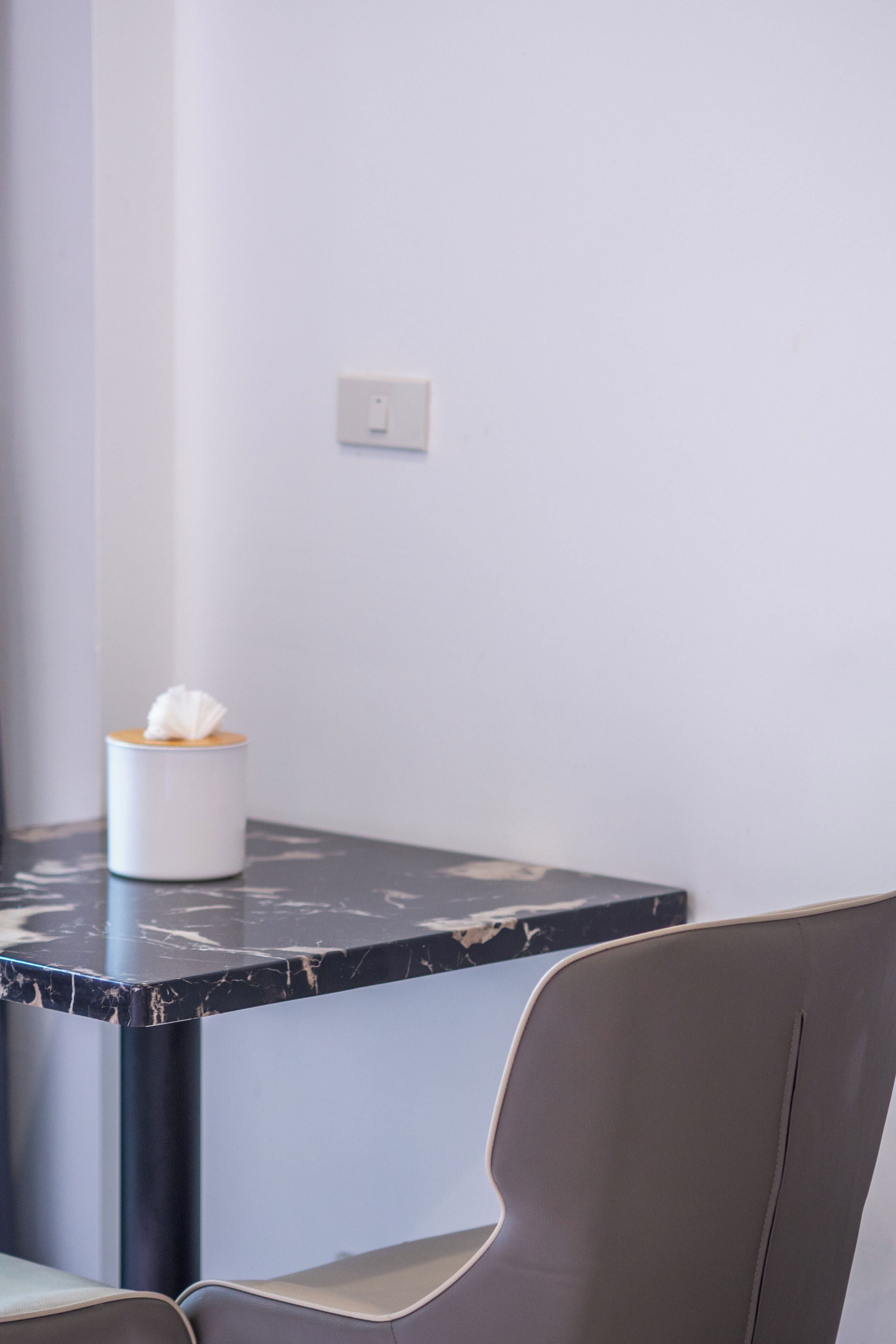 A modern room with a marble table, a white tissue box, a grey chair, and a light switch on the wall.