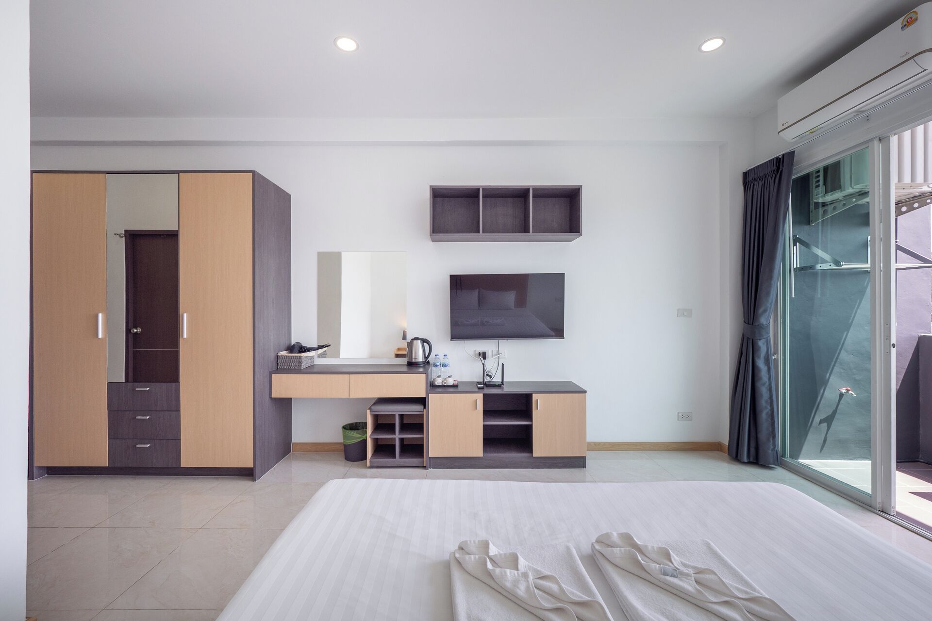 Ett modernt hotellrum med en säng, en garderob, en sminkbord med spegel, en TV och ett stort fönster.