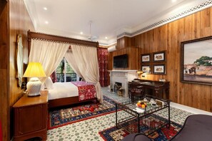 Een slaapkamer met een hemelbed, een bureau, een open haard en een groot gepresenteerd schilderij aan de muur.