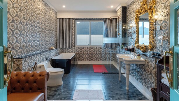 Un baño con bañera, inodoro y lavamanos, con papel tapiz estampado y un espejo grande.