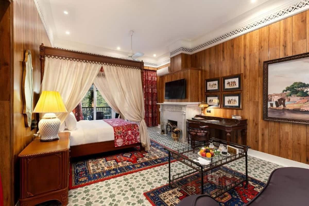Une chambre à coucher avec un lit à baldaquin, un bureau, une cheminée et un grand tableau encadré au mur.