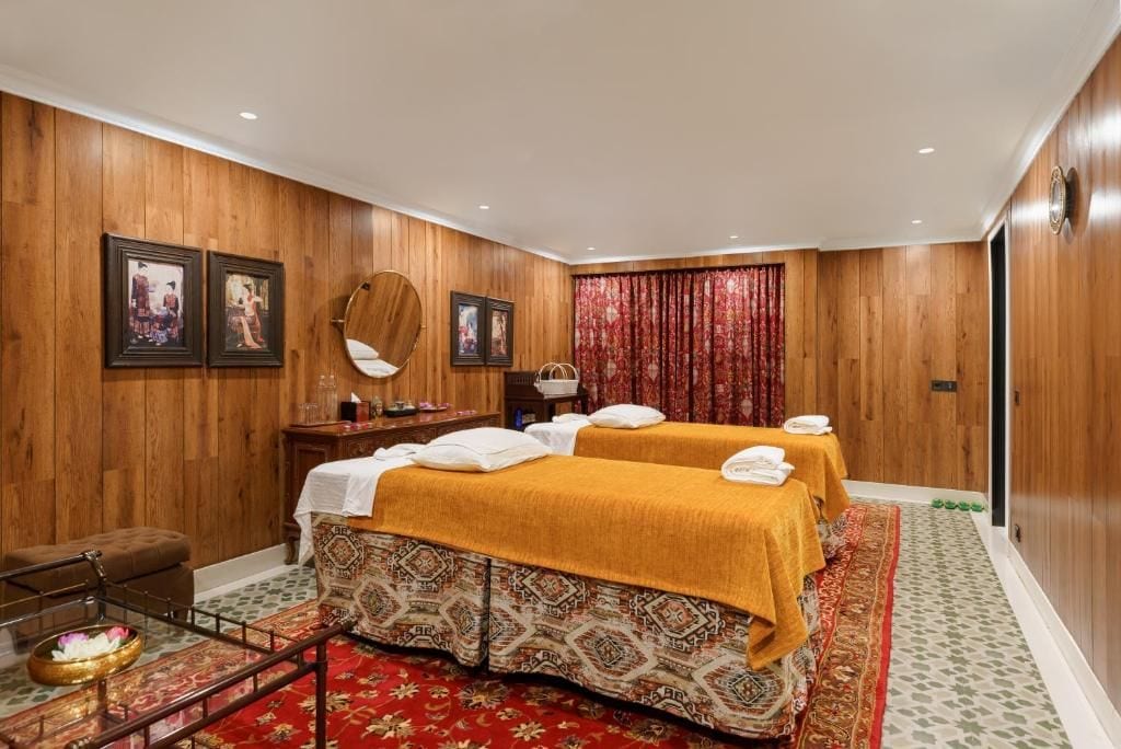 A hotel room with wooden paneling, two beds with yellow linens, a small table with a mirror, and a red curtain.