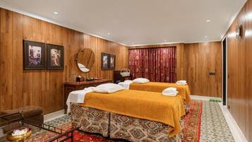A hotel room with wooden paneling, two beds with yellow linens, a small table with a mirror, and a red curtain.