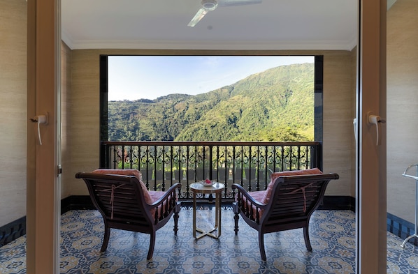 Un balcon avec deux chaises et une petite table, une vue sur un paysage montagneux et des carreaux de sol à motifs.