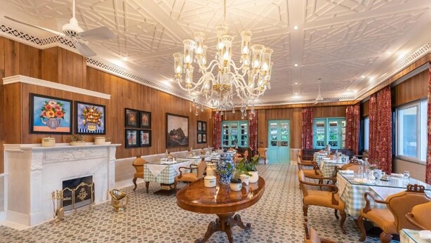 Een eetruimte met meerdere tafels, een kroonluchter en lijstwerken aan de wanden.