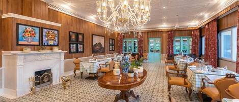 A dining area with multiple tables, a chandelier, and framed artwork on the walls.