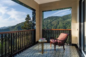 Un balcon donnant sur un paysage montagneux, une petite table ronde avec un saladier, et une chaise rouge avec un coussin.