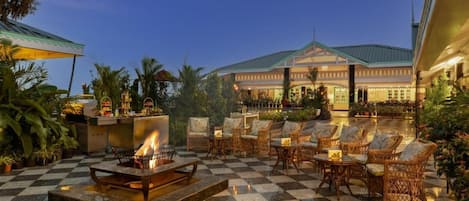 A checkered outdoor seating area with a fire pit, wicker chairs, and a building in the background.