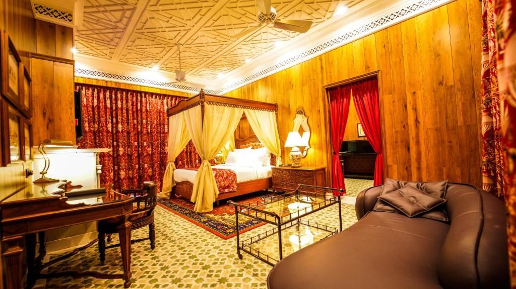 A traditional room with a four-poster bed, a desk, a massage chair, and a piano.