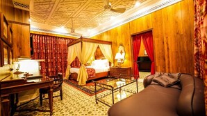 Una habitación tradicional con una cama con dosel, un escritorio, una silla de masajes y un piano.