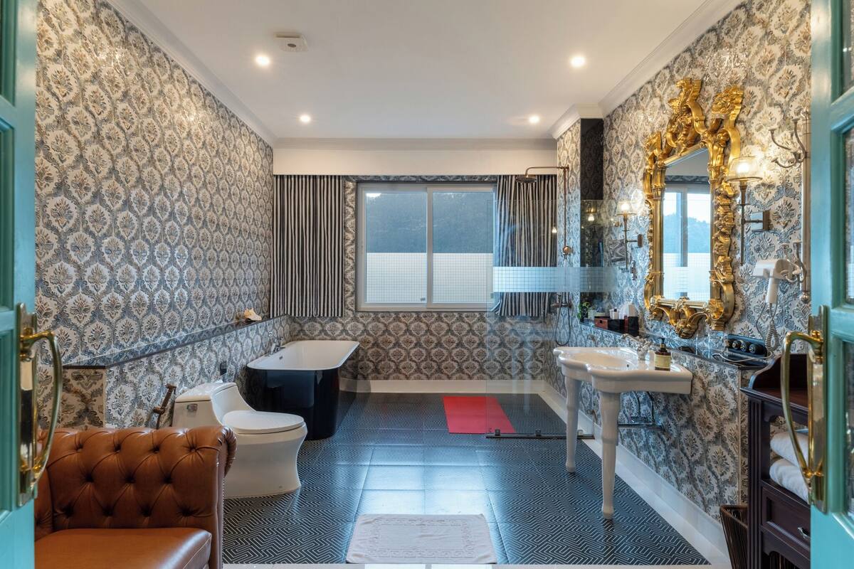 Une salle de bain équipée d’une baignoire, de toilettes et d’un lavabo, avec un papier peint à motifs et un grand miroir.