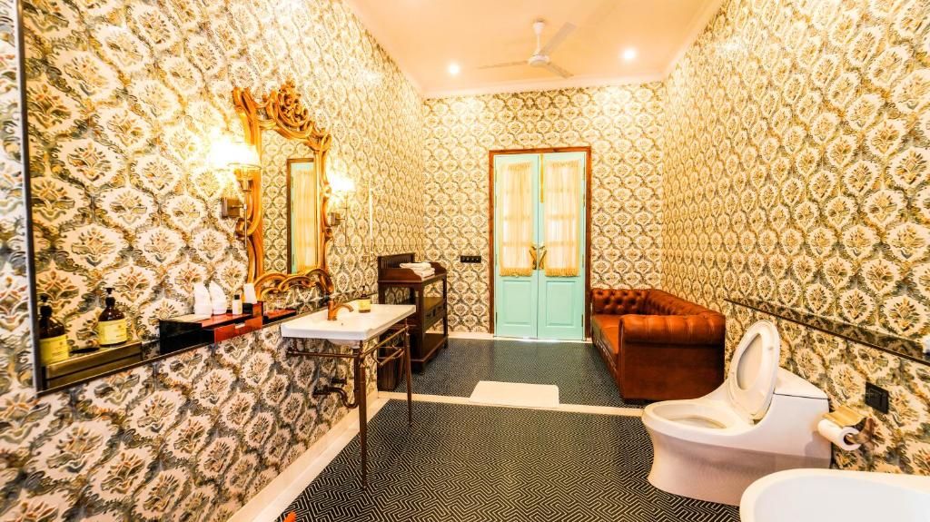 A bathroom with patterned wallpaper, a toilet, a sink, a mirror, and a ceiling fan.