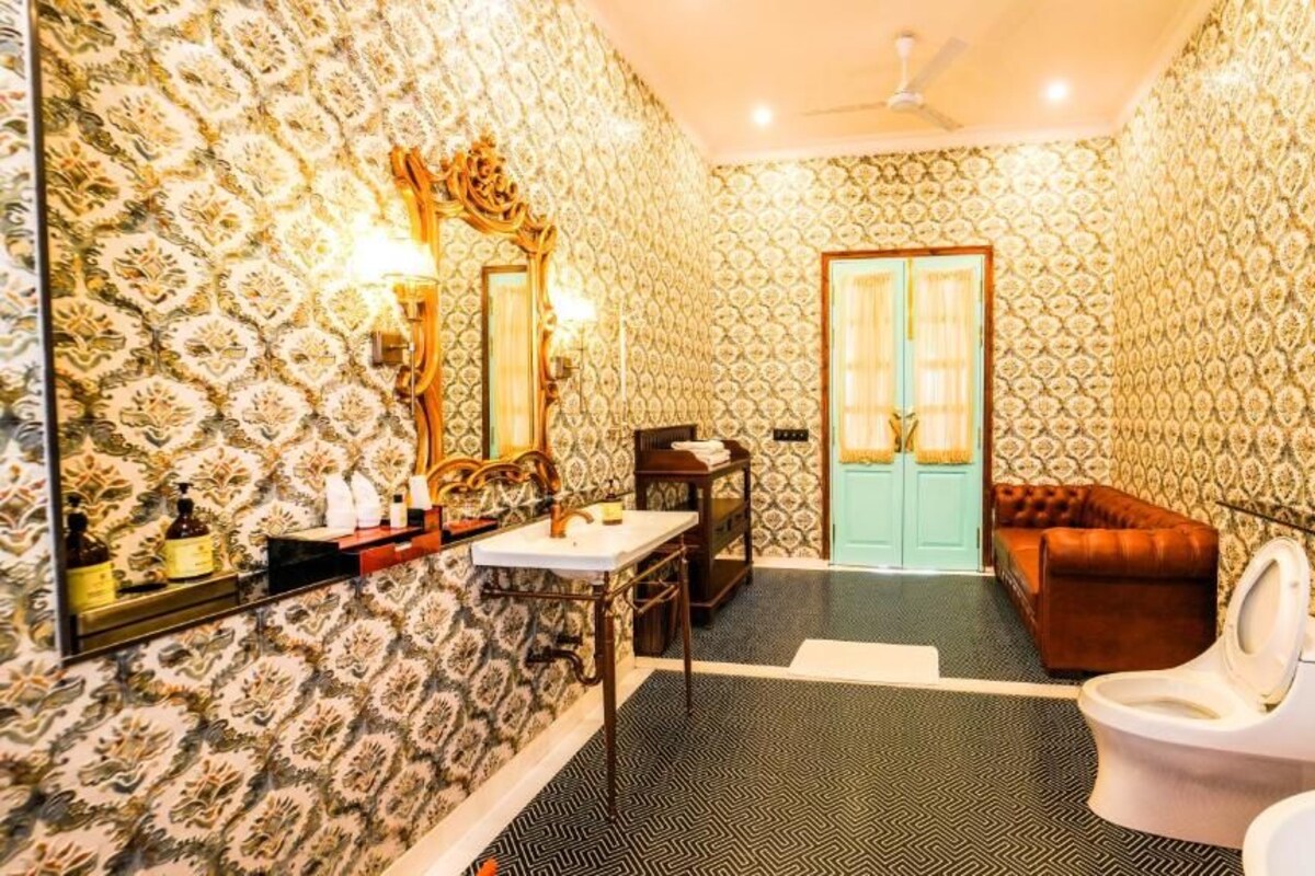 Uma casa de banho com papel de parede estampado, sanita, lavatório, espelho e ventoinha no teto.